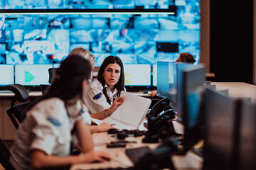 Group of Security data center operators working in a CCTV monitoring room looking on multiple...