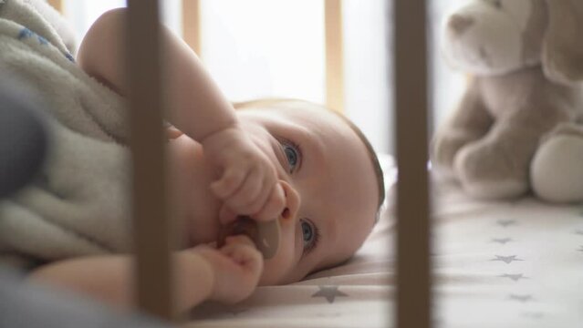 9 months baby chewing pacifier in his crib. Close up of toddler face.
