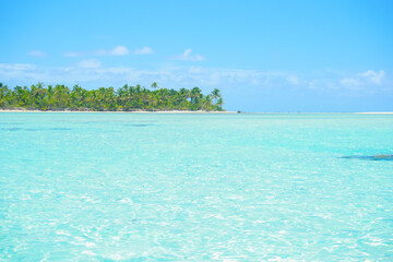 Typical tropical South Pacific scene heat haze over turquoise water, low atoll island on horizon blue sky and white coulds