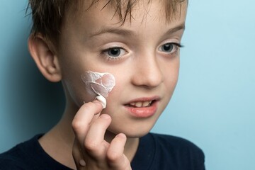 a little boy smears cream on his face.