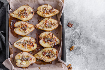 Delicious baked pear with dorblu cheese, walnut and honey on a textured concrete background