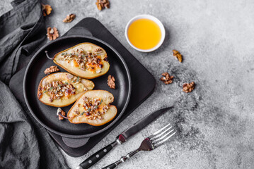 Delicious baked pear with dorblu cheese, walnut and honey on a textured concrete background