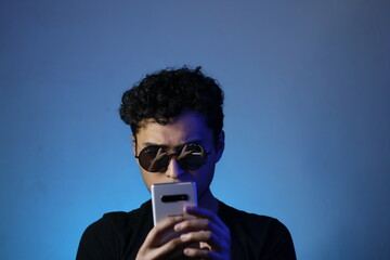 joven latino viendo su teléfono inteligente posando en un fondo azulado