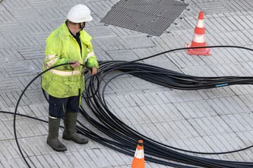 Worker handling a communication cable on the sidewalk of a city