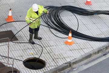 Worker handling a communication cable on the sidewalk of a city