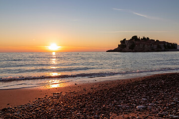 Scenic sunset view from Sveti Stefan Beach at Adriatic Mediterranean Sea, Budva Riviera, Montenegro, Europe. Reflection of sun beams on water surface during twilight. Summer vacation in seaside hotel