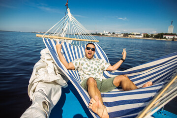 Handsome man rests in a hammock on a yacht. Leisure and fun in a water