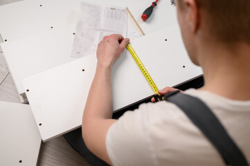 Furniture assembler measures a wooden board with a tape measure, close-up. Construction concept, handyman