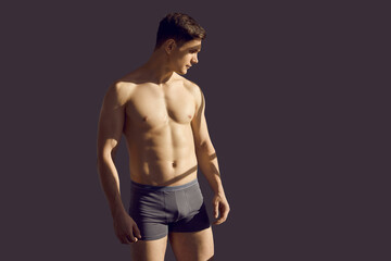 Fototapeta premium Sporty sexy young man in underwear isolated on black studio background. Toned fit male model in underclothing wear advertise good quality clothing. Body shape and fitness concept.