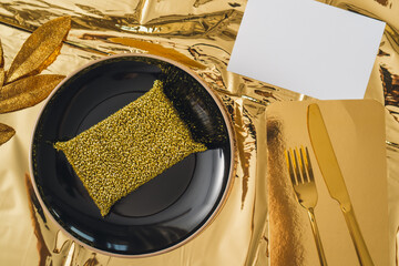 Gold metal wash sponge on black plate, gold knife and fork, gold tablecloth, ironic concept of gold...
