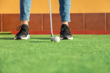 Close-up of unrecognizable woman hitting ball with golf club in mini golf