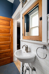 A small half bathroom with a white pedestal sink mounted on the wall with a wood framed medicine cabinet mirror above and a towel hook to the side.