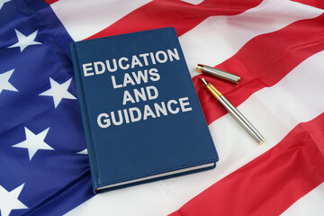 On the US flag lies a pen and a book with the inscription - EDUCATION LAWS AND GUIDANCE
