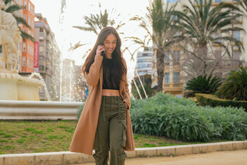 Fototapeta premium Young woman talks through her mobile phone on the street at sunset
