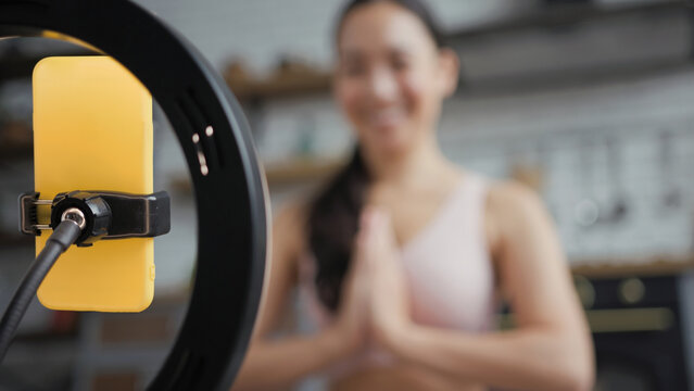 Healthy asian yoga woman sitting in lotus position and doing online yoga lesson. Focus on phone. Namaste