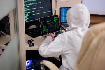 Boy hacker fraudulently use credit card for payment. Internet theft . Man wearing a balaclava and holding a credit card while sat behind a laptop.