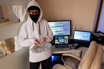 Boy hacker with money dollars. Internet theft . Man wearing a balaclava behind a laptop.
