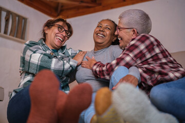 Fototapeta premium Three middle-aged women gather in the living room of the house by the fireplace with an affectionate attitude. Concept: friendship, tea time, home