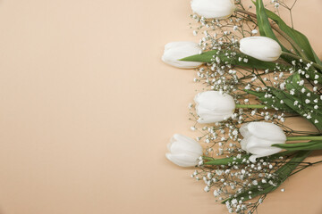 White tulips and gypsophila flowers bouquet on a beige background. Mothers Day, birthday celebration concept. Copy space for text. Mockup
