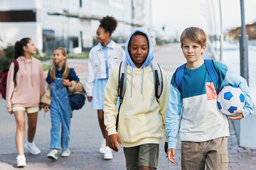 Group of intercultural adolescent secondary school learners in casualwear walking along street...