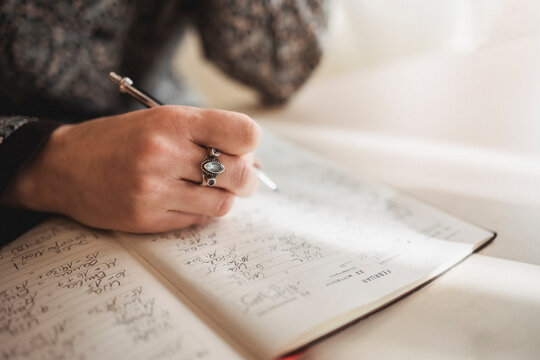 Closeup Of Woman Hand With Beautiful Ring Writing In A Notebook With A Pencil. Making Schedule Manually.