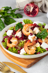 Salad with shrimps, pineapple, feta and pomegranate seeds in a plate on green lettuce leaves, on wooden board