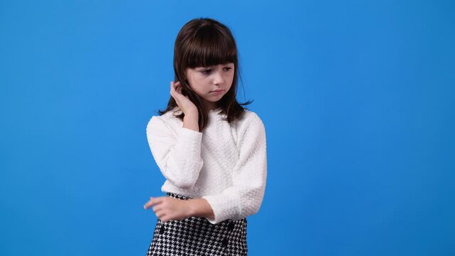 4k video of one young girl who touches her hair and thinks about something with a negative expression over blue background.