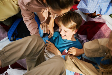 Above angle of youthful boy in casualwear surrounded by his playful friends lying on plaid and...