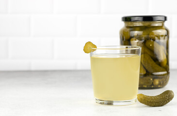 Pickle juice or brine in a glass and jar of pickled cucumbers on a white background. Copy Space. 