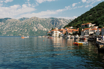 Fototapeta na wymiar Boats moored at the pier of Perast with old houses at the foot of the mountains
