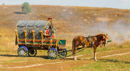 a horse harnessed to a festively decorated wagon against the background of a field without people