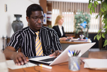 Concentrated african american businessman working with laptop and papers at office desk