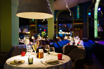 a table with a white tablecloth, glasses, crockery and decor in dark restaurant
