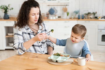 Adorable toddler boy refuses to eat vegetables that his mother offers him. A young mother worries...