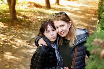 Fototapeta premium Mother and teenage daughter are happy in the park, taking pictures, hugging and talking. With the help of the mother, the daughter passes the teenage period easily