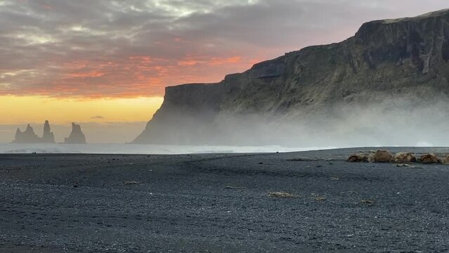 Sunset on Black Sand Beach Vik, Iceland. Reynisdrangar cliffs and sea stacks. Views of the cliffs and stone stack from Vik near Ring Road.