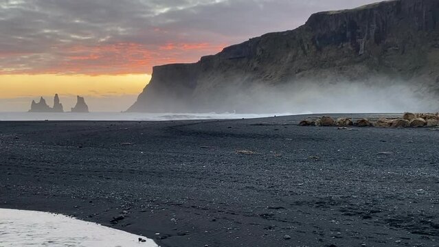 Sunset on Black Sand Beach Vik, Iceland. Reynisdrangar cliffs and sea stacks. Views of the cliffs and stone stack from Vik near Ring Road.