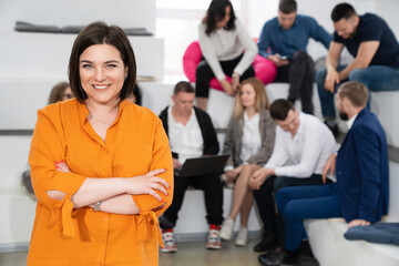 a brunette woman in an orange blouse with men and women in the office.