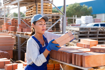 Asian female construction shop worker stacks bricks on an open-air site