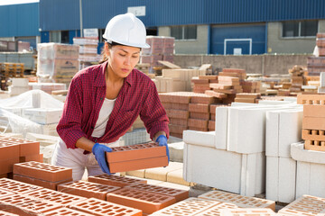 Attentive asian woman working in an open air building materials warehouse is laying bricks