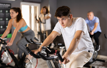 Sportive people in activewear warming up on training using exercise bike in gym
