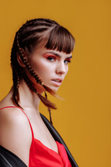 Portrait of a beautiful woman model in a red dress with braids and bright makeup. Model portrait of...