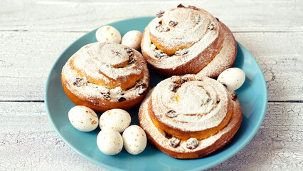 Easter decor with sugar flowers and chocolate eggs with round spiral buns on a blue plate