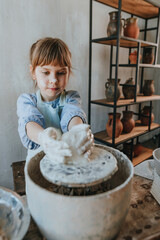 Little girl working with clay on potter's wheel