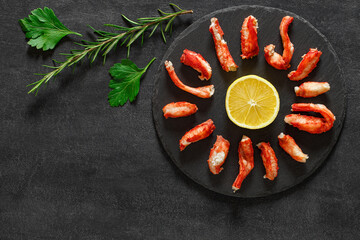 Crab meat sliced, cut yellow lemon green parsley and rosemary on slate stone plate round, dark background, top view, space to copy text.