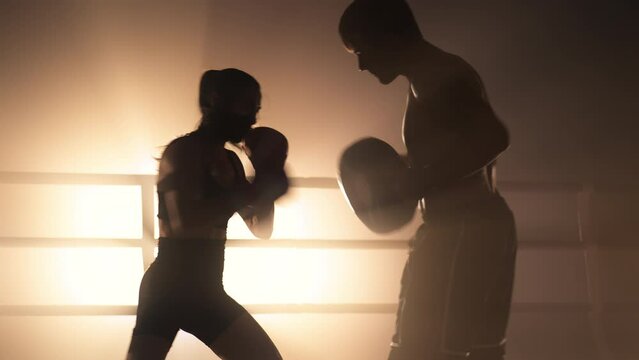 Close-up shot of a woman working out with a personal trainer in the boxing ring. Portrait of sporty couple building muscle strength and burning calories in the gym. High quality 4k footage