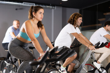 Fototapeta na wymiar Men and woman taking indoor cycling class at fitness center, doing cardio riding bike