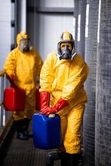 Hardworking employees in protective equipment and gas masks carrying chemicals inside production plant.