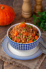 Pumpkin Buckwheat Porridge Bowl. Buckwheat stew or kasha with sauteed butternut squash, onion, tomato, garlic and herbs served in a bowl. Wooden background, selective focus, vertical.