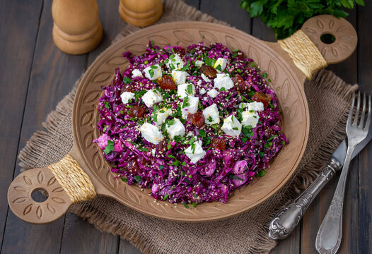Shredded Red cabbage salad with dates, feta cheese, herbs, toasted sesame seeds and lemon-olive oil dressing. Dark wooden background, selective focus, horizontal.